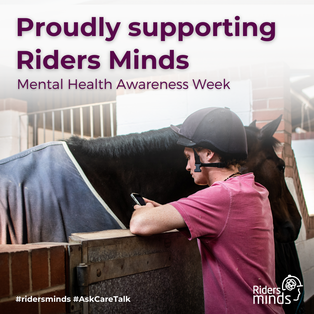 A male rider wearing a riding hat and a pink t-shirt leans against a stable door while looking at his phone. In the background, a dark horse wearing a blue rug stands in the stable. The text overlay reads 'Proudly supporting Riders Minds' and 'Mental Health Awareness Week.'
